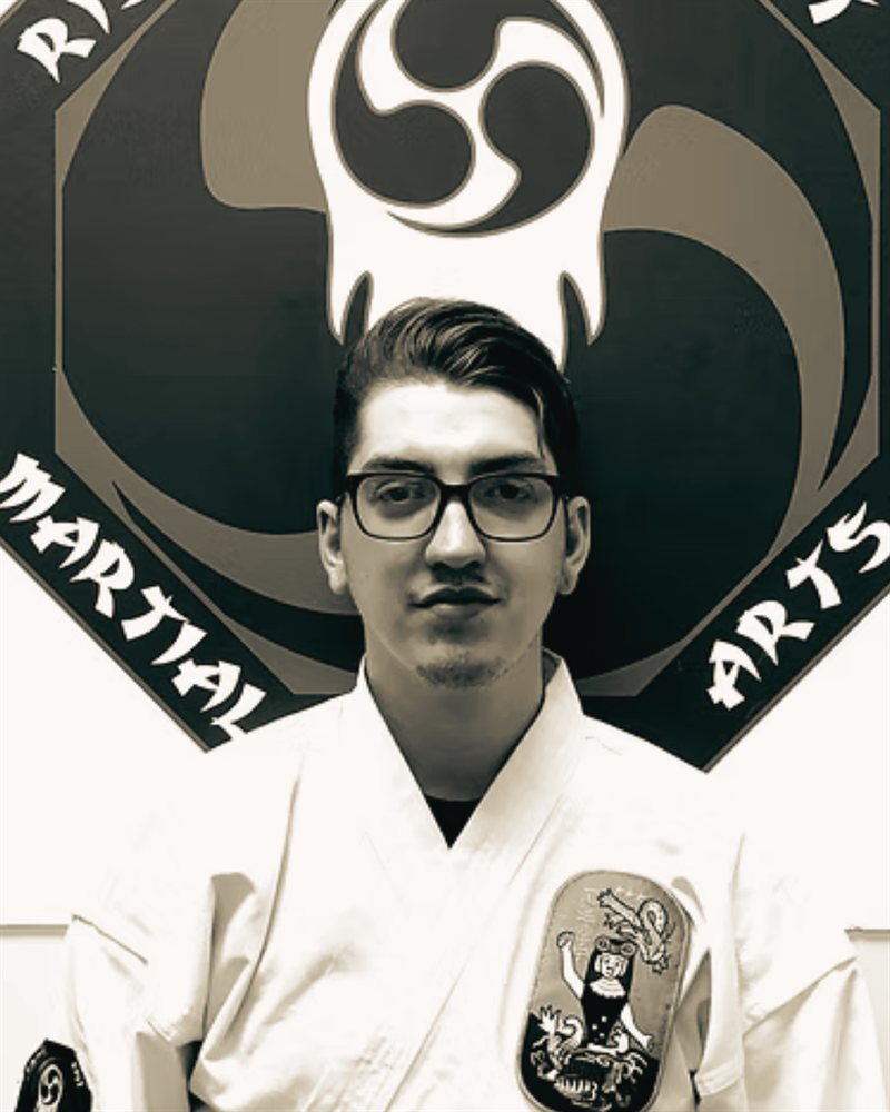 Jesse Fearfield, Head Instructor and owner, in a gi in front of the Rising Fist Martial Arts logo